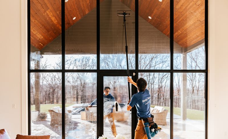 Professional window cleaner servicing a modern Tulsa home with floor-to-ceiling windows