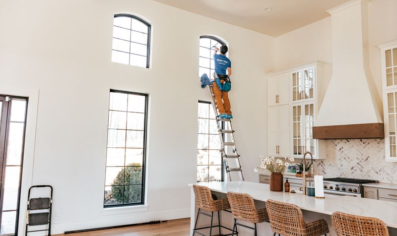 Better View team member on a ladder cleaning high windows in a kitchen